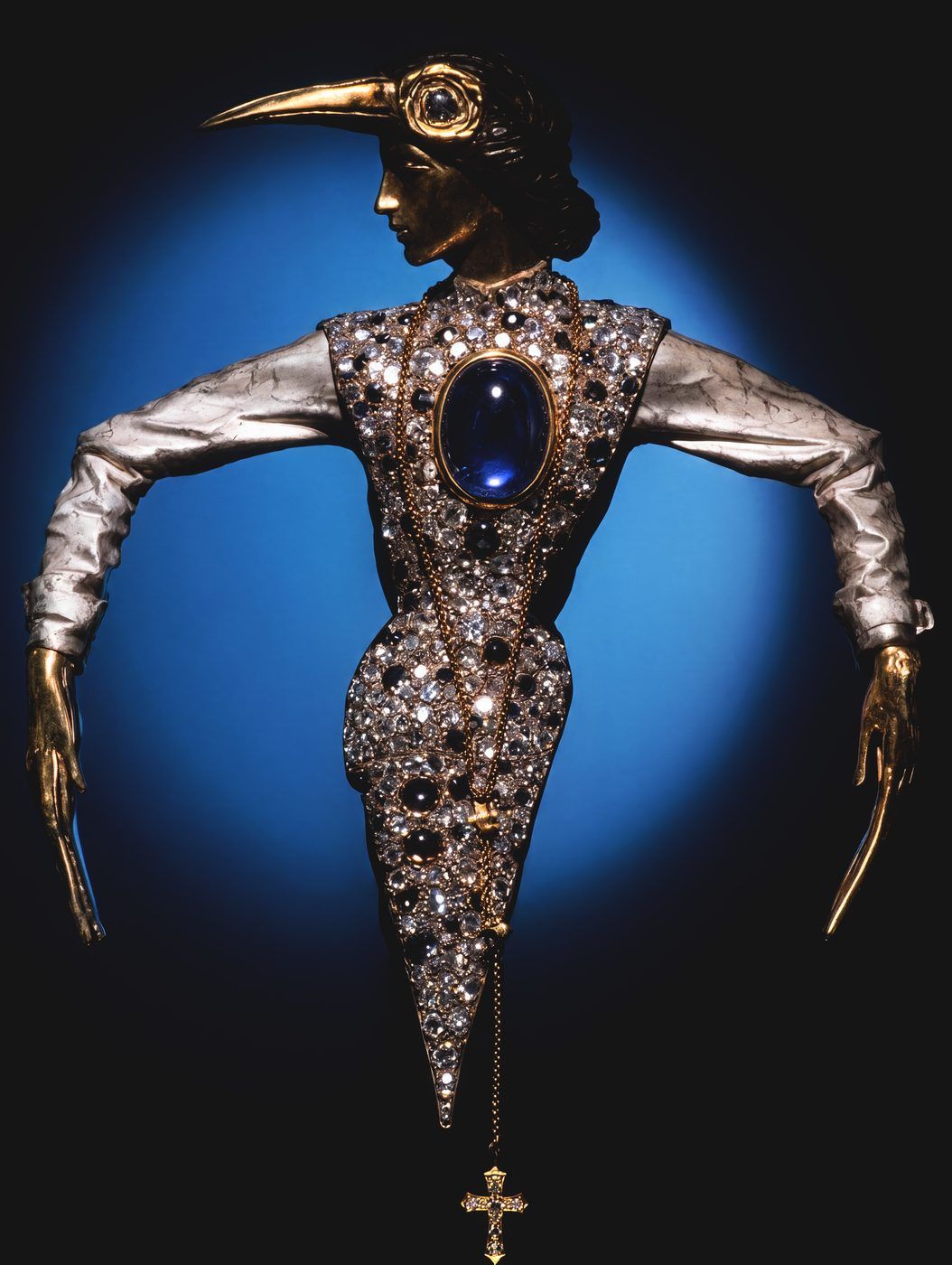 Bird of Pray Brooch by Nilofar — a gold figure crowned with a bird-beak headdress, set with a blue cabochon sapphire and diamonds, a one-of-a-kind fine jewelry piece